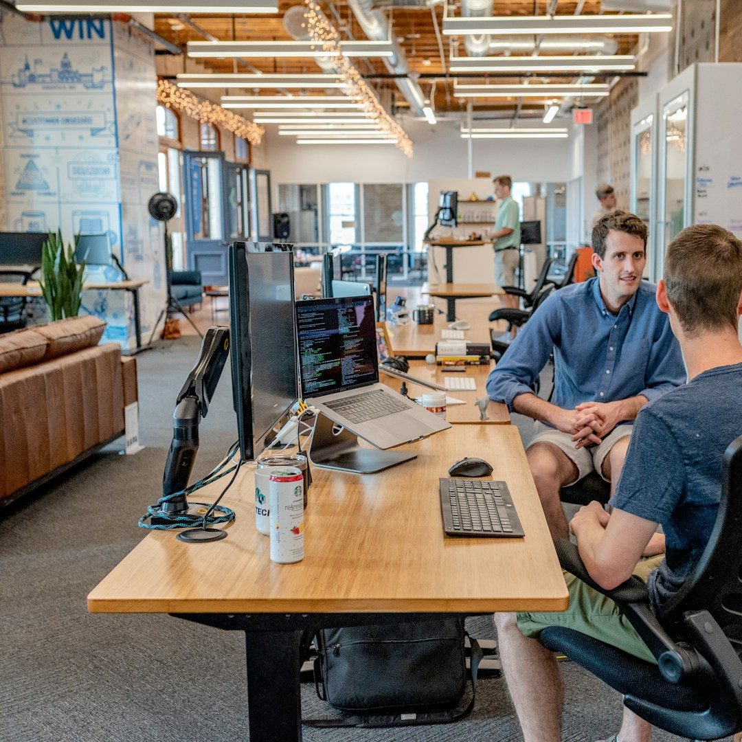 Le Numérique Deux personnes discutent dans un bureau moderne avec des équipements informatiques.