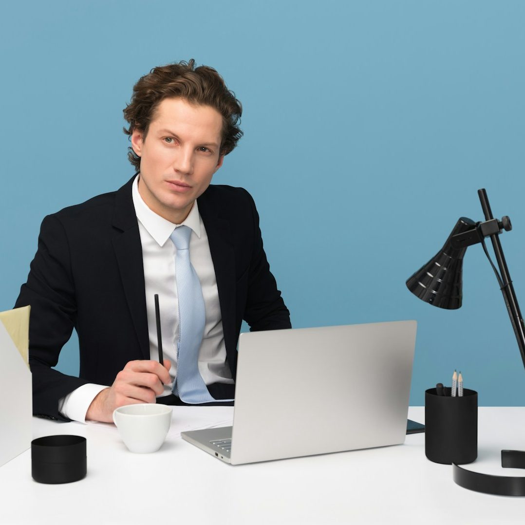 soutien informatique Homme en costume assis à un bureau moderne, regardant l'objectif avec un ordinateur portable.