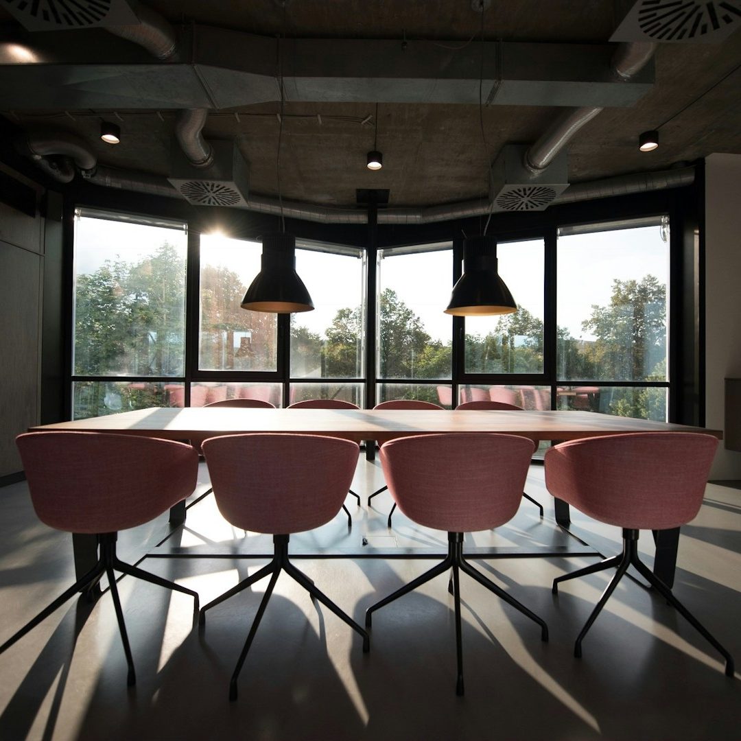 accompagnement de projet Salle de réunion moderne avec une table et des chaises roses, grandes fenêtres, éclairage pendentif.